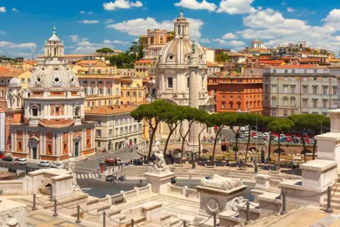 Vista panoramica di Roma con l'Altare della Patria in primo piano, cupole imponenti e palazzi storici sotto un cielo azzurro con nuvole bianche.