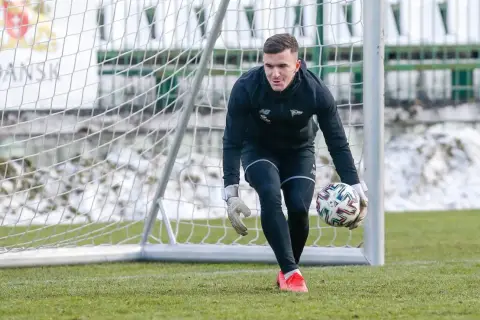 Młody bramkarz piłkarski w czarnym stroju z rękawicami na dłoniach trzyma piłkę, gotowy do akcji.