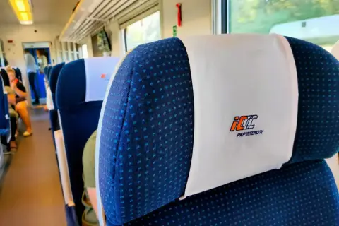 Wnętrze pociągu PKP Intercity. Siedzenia z zagłówkami, na których widnieje logo przewoźnika. Czy bilet PKP z rezerwacją miejsca czy bez – kiedy warto dopłacić?