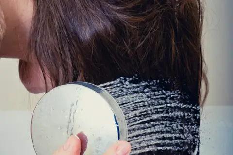 Duschkopf mit Wasserstrahlen, die auf braunes Haar treffen. Ein Hauch von Reiswasser für gesunde Haare.