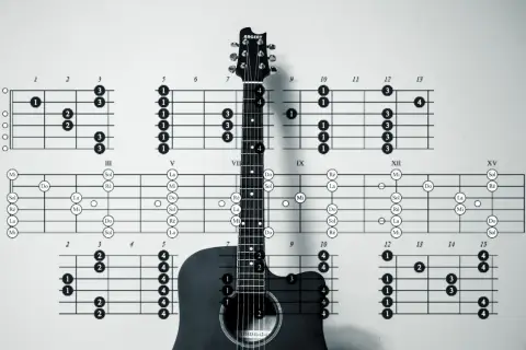 Akustyczna gitara na tle diagramów akordów, w tym akord E. Nauka gry na gitarze.