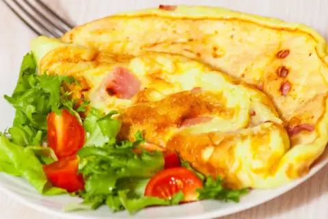Złocisty omlet z szynką i pomidorkami koktajlowymi na talerzu z sałatą.