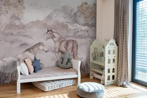 Urocza tapeta w koniki zdobi pokój dziecka. Na ścianie widać konie w biegu i odpoczywające, w otoczeniu gór i drzew.