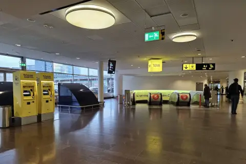 Żółte automaty biletowe Arlanda Express i schody ruchome prowadzące do pociągu.