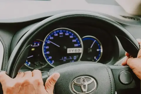Ręce na kierownicy Toyoty, widoczne zegary i wskaźniki. Elektryczne wspomaganie kierownicy ułatwia jazdę.