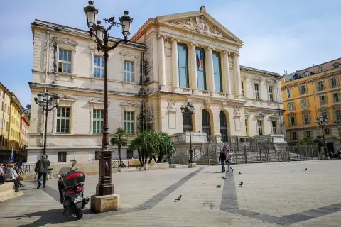 Plac przed Pałacem Sprawiedliwości na Cours Saleya. Skuter, latarnie i gołębie na brukowanym placu.