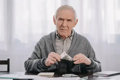 Starszy mężczyzna z portfelem w ręku, zastanawia się, kiedy na wcześniejszą emeryturę po nowemu.