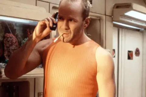 Bruce Willis jako Korben Dallas, jeden z bohaterów "Piątego elementu", rozmawia przez telefon z papierosem w ustach.