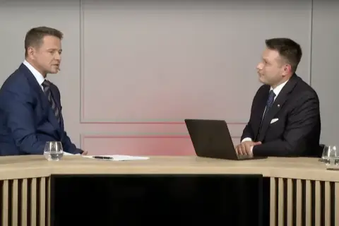 Sławomir Mentzen w garniturze siedzi przy biurku z laptopem, rozmawiając z drugim mężczyzną. Czy to dowód, dlaczego Sławomir Mentzen unika debat z kandydatami Koalicji Obywatelskiej?
