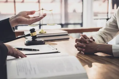 Prawnik omawia z klientem formalności związane z wnioskiem o stwierdzenie nabycia spadku. Na stole leżą dokumenty, młotek sędziowski i waga sprawiedliwości.