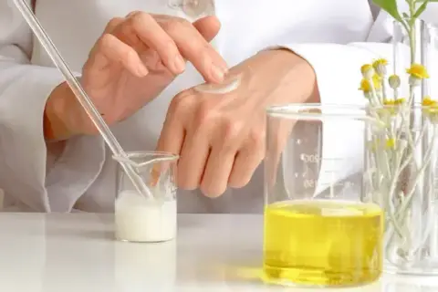 Manos de científico aplicando crema, con probetas y plantas. El cetearyl alcohol es clave en esta formulación.