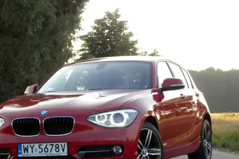 Czerwone BMW 118d na tle drzew i pól.