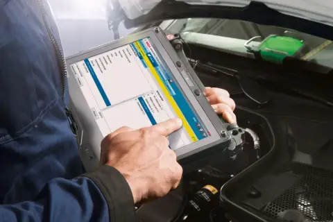 Mechanik sprawdza wtryski za pomocą tabletu diagnostycznego Bosch. Na ekranie widoczne są opcje wyboru systemu, w tym silnik i systemy sterowania.
