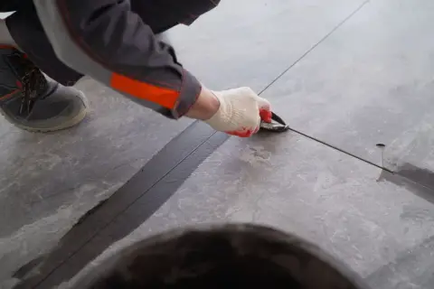 Pracownik w rękawiczkach nakłada ciemną fugę na taras zewnętrzny, tworząc estetyczne i trwałe połączenie.