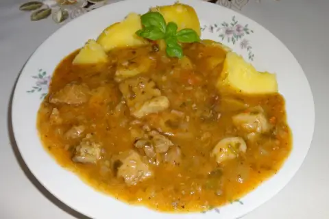 Pyszny sos do ziemniaków z kawałkami mięsa i warzyw, udekorowany listkiem bazylii.