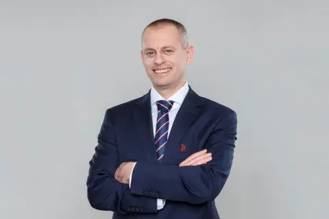 Marcin Włodarski, trener, w granatowym garniturze i krawacie, z rękami skrzyżowanymi na piersi, uśmiecha się do obiektywu.
