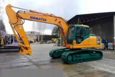 Pomarańczowa koparka gąsienicowa Komatsu PC 180 LC z zielonym podwoziem stoi na placu budowy.