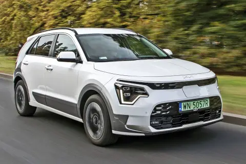 Biały Kia e-Niro jedzie po drodze, otoczony zielenią drzew.