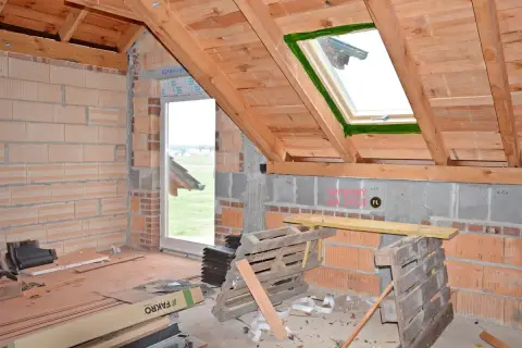 Wnętrze domu w budowie, widoczne połaciowe okno dachowe i ściany z pustaków.