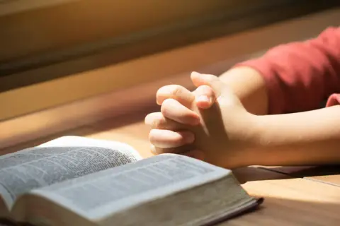 Dziecko z złożonymi dłońmi nad otwartą Biblią. To obraz modlitwy za córkę, pełen nadziei i wiary.