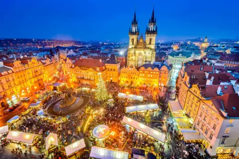 Tłoczny jarmark bożonarodzeniowy w Pradze, z oświetloną choinką i zabytkową architekturą w tle.