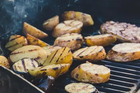 Pommes de terre coupées en quartiers, grillées à la perfection sur un barbecue, dégageant une fumée alléchante. Quelle pomme de terre barbecue !
