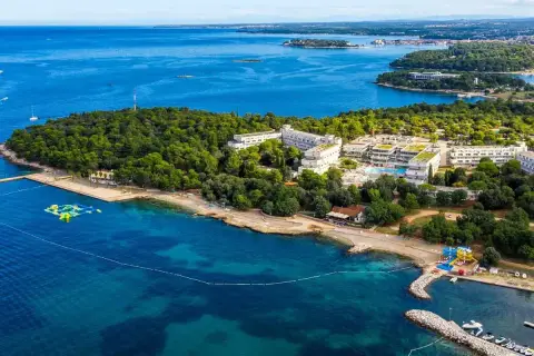 Hotel Delfin Plava Laguna, otoczony zielenią, z basenami i plażą nad turkusowym morzem.