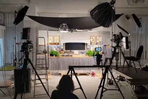 Studio filmowe z kuchnią, kamerami i lampami. Widać tu moc światła, które tworzy atmosferę do nagrania.