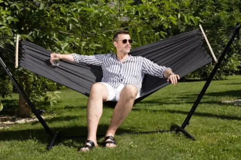Mężczyzna w okularach relaksuje się w czarnym hamaku na trawie. Idealny wybór, by odpocząć w ogrodzie.