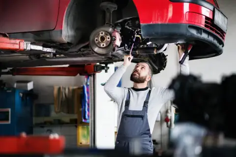 Mechanik w warsztacie sprawdza podwozie czerwonego samochodu na podnośniku.