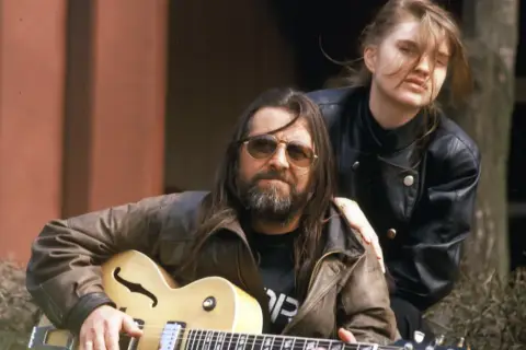Grażyna Dramowicz biografia: muzyk z gitarą i młoda kobieta w skórzanej kurtce.