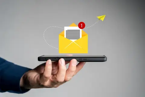 Dłoń trzyma smartfon, z którego wylatuje żółta koperta z powiadomieniem. Pomysł na to, co napisać w SMSie o urlop na żądanie.