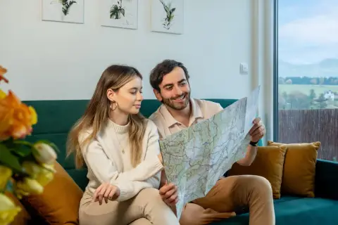 Para planuje podróż, przeglądając mapę. W tle widać krajobraz z domkami, przypominający widok z **Osolina**.