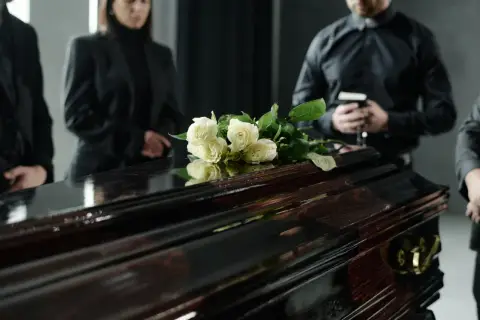 Białe róże na ciemnej trumnie, ludzie w żałobie. Wskazówki, jak zachować się na pogrzebie, w tym szacunek i powaga.