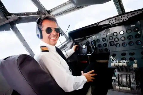 Uśmiechnięty pilot w okularach przeciwsłonecznych i słuchawkach w kokpicie samolotu. Zastanawiasz się, ile zarabia pilot samolotu?