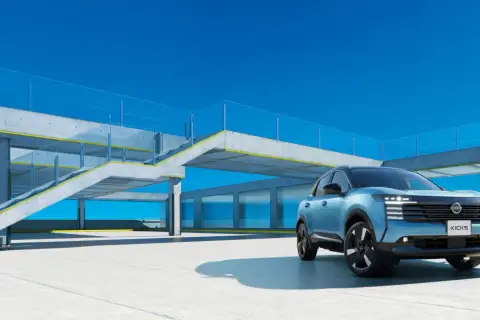 Niebieski Nissan Kicks stoi na betonowym placu przed nowoczesnym budynkiem z przeszklonymi oknami i betonowymi schodami.