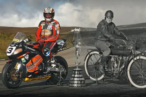 Conor Cummins junto a su moto de carreras y un trofeo, junto a un piloto histórico en una Indian.