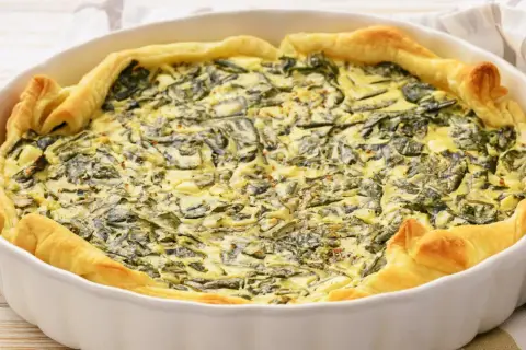 Pyszny quiche ze szpinakiem w białej formie, idealny pomysł na to, jak jeść szpinak. Złociste ciasto i kremowe nadzienie.