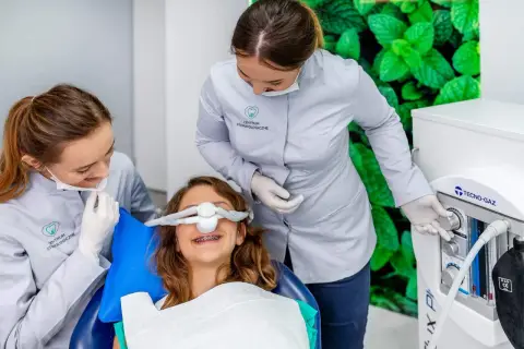 Uśmiechnięta dziewczynka z aparatem na zębach otrzymuje gaz rozweselający od dentystki, która obsługuje aparat.