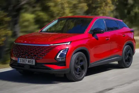 Czerwony, nowoczesny SUV, jeden z chińskich samochodów elektrycznych, jedzie po drodze wśród drzew.