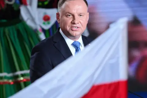 Prezydent Andrzej Duda z polską flagą, w tle ludowy strój. Może to symbolizować ułaskawienie i dumę narodową.