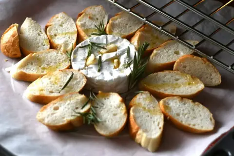 Pyszny, pieczony camembert z czosnkiem i rozmarynem, otoczony kromkami bagietki. Idealna przekąska na ciepło.