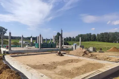Budowa domu w toku. Widać fundamenty, betonowe słupy i hałdy piasku, który czeka na zagęszczenie.