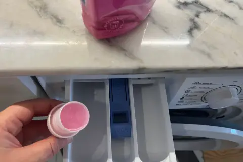 Hand hält Dosierkappe mit rosa Flüssigkeit. Waschpulver direkt in die Trommel geben? Nein, hier in die Schublade.