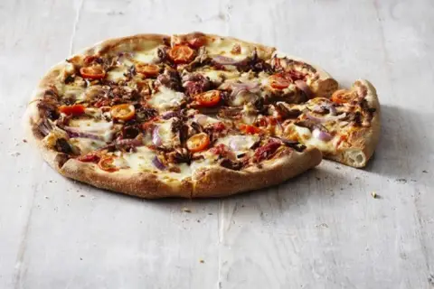 Pizza Hut ciasto San Francisco z pomidorkami, cebulą i serem. Pyszna, gorąca pizza na drewnianym blacie.