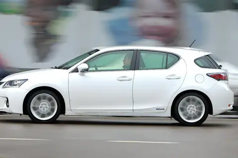 Biały Lexus CT200h w ruchu ulicznym, z rozmytym tłem i innymi samochodami.
