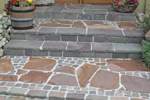 Stufen mit polygonalplatten verlegen. Große, unregelmäßige Steinplatten wechseln sich mit kleinen, quadratischen Pflastersteinen ab.