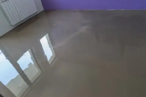 Lśniąca, świeża wylewka w neutralnym kolorze, odbijająca światło okien.
