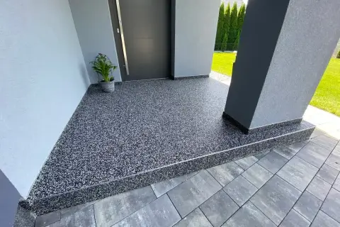 Nowoczesny kamienny dywan koszt 1m2 przy wejściu do domu. Elegancka, szara posadzka z drobnym kamyczkiem.