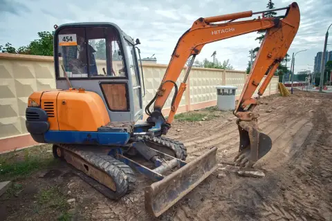 Pomarańczowa koparka Hitachi z gąsienicami i szerokim lemieszem do koparki, gotowa do pracy na budowie.